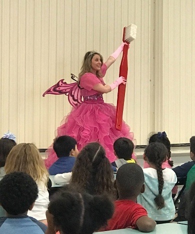 Dental team member dressed as tooth fairy holding oversized toothbrush while talking to Wylie children