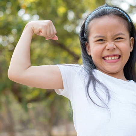 A young girl wearing a white shirt and showing off her muscles gives a big smile in Wylie
